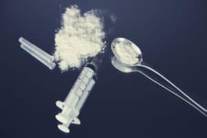 Fentanyl and heroin in powder form next to a syringe and a spoon