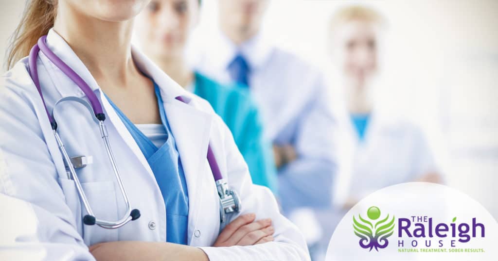 A doctor stands in front of a team of other medial professionals, with a stethoscope around her neck.