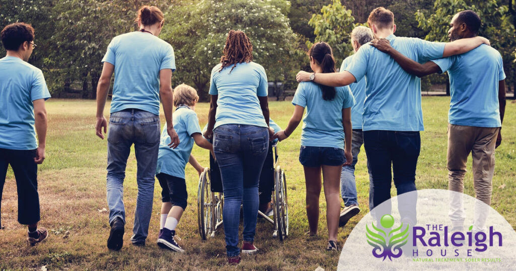 A group of volunteers links arms as they walk through a grassy field.