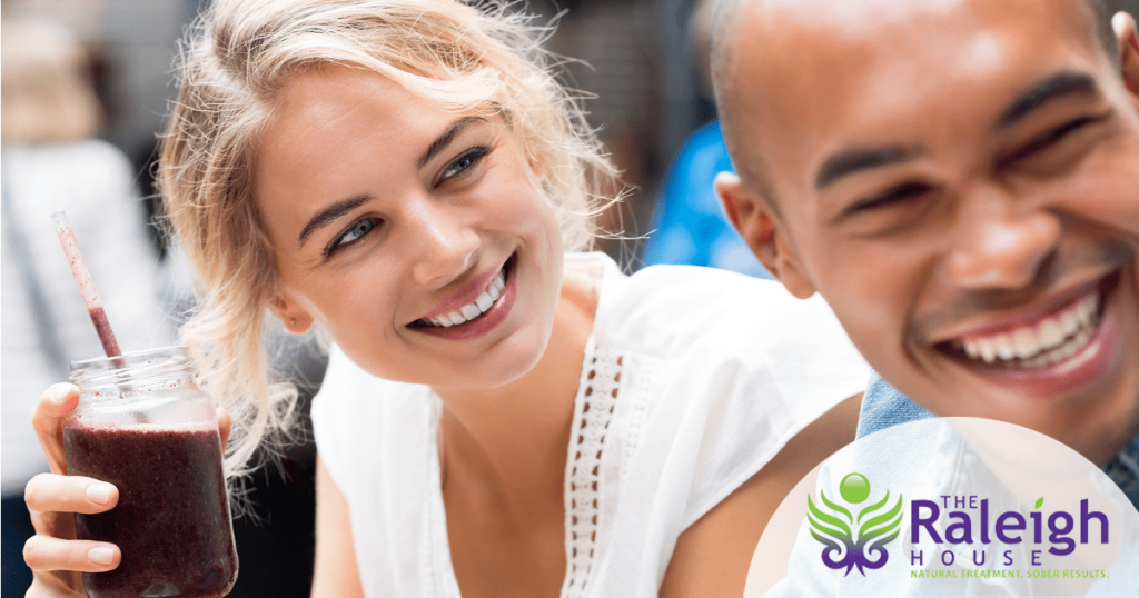 A young man and woman, who is drinking a smoothie, sit together looking happy and healthy.