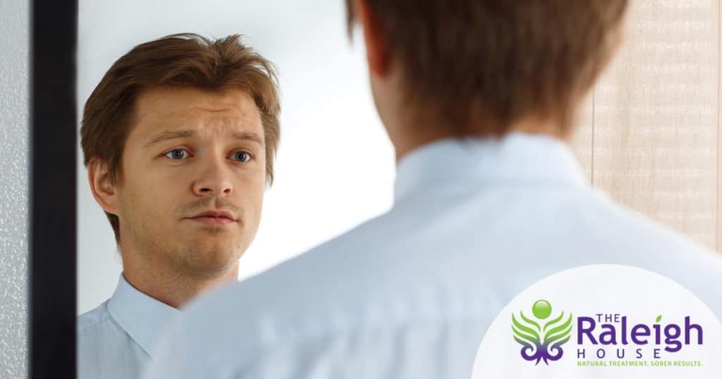 A young businessman looks in a mirror with a pensive expression on his face.