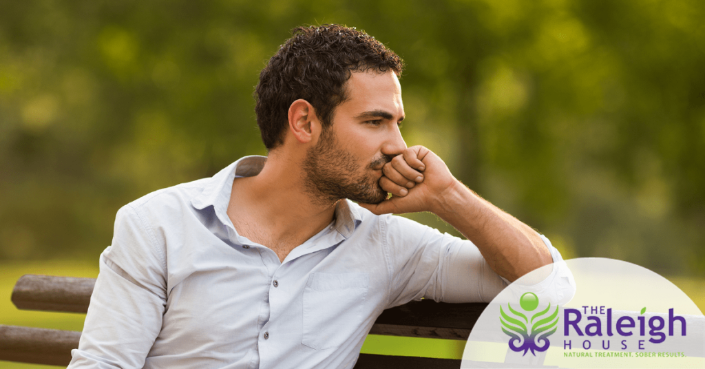 A young man struggling with heroin addiction and depression sits on a park bench, deep in thought.