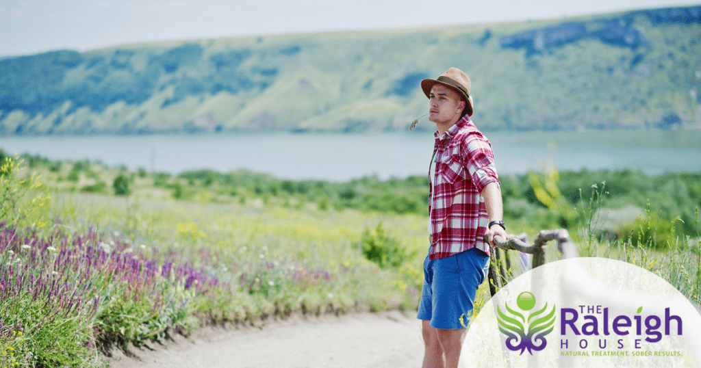 A young man in shorts and a hat takes a walk in the countryside.
