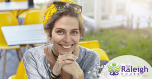 A happy woman sits outside on a yellow bench near fresh flowers.