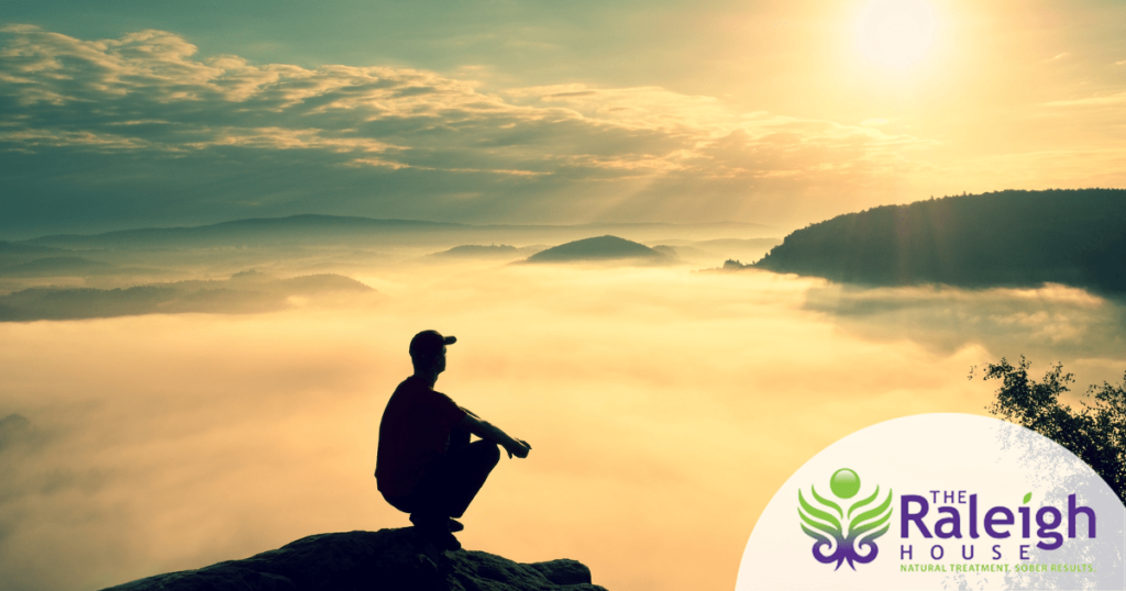 A man sits on a rock and watches the mist float over a valley.