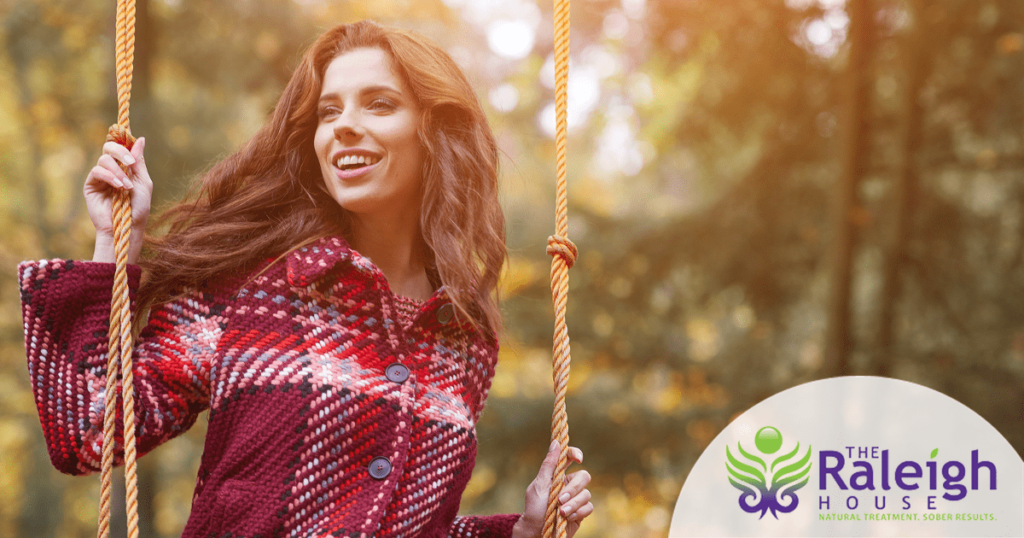 A woman sits on a swing in the park with the beauty of the fall foliage behind her.