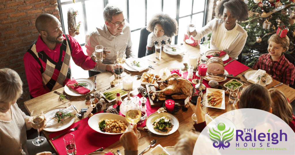A family gathers around a table laden with food and shares a toast with a Christmas tree in the background. 