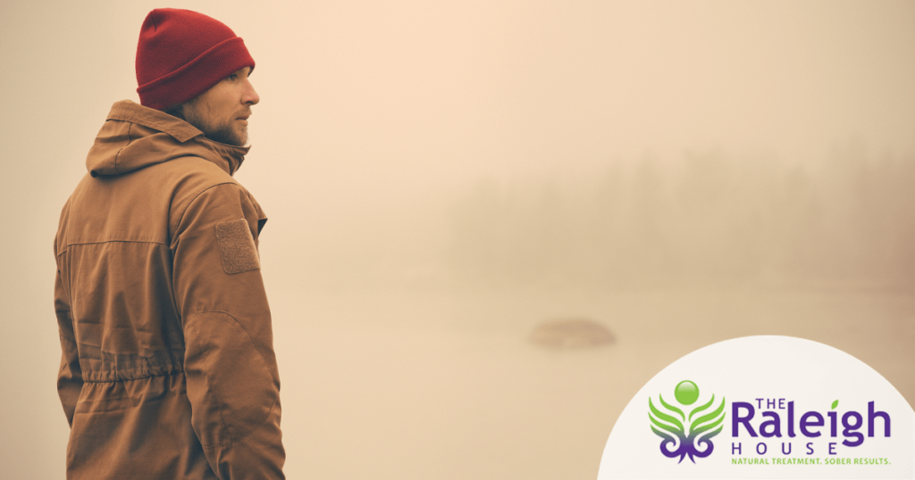 A young man stands alone outside on a foggy day.