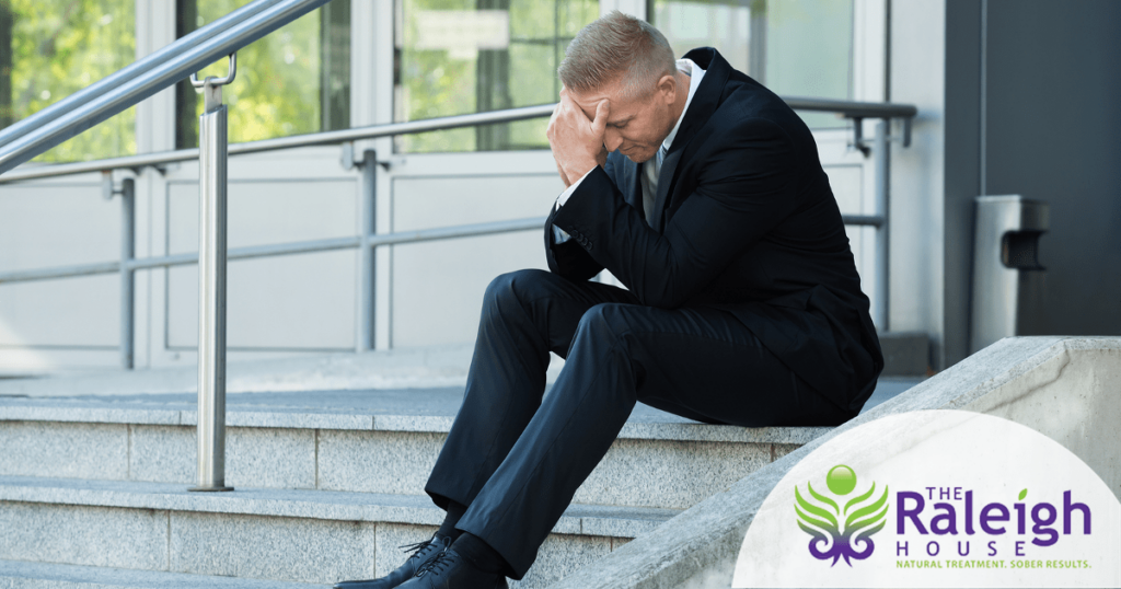 A businessman sits on the steps outside his office with his head in his hands.