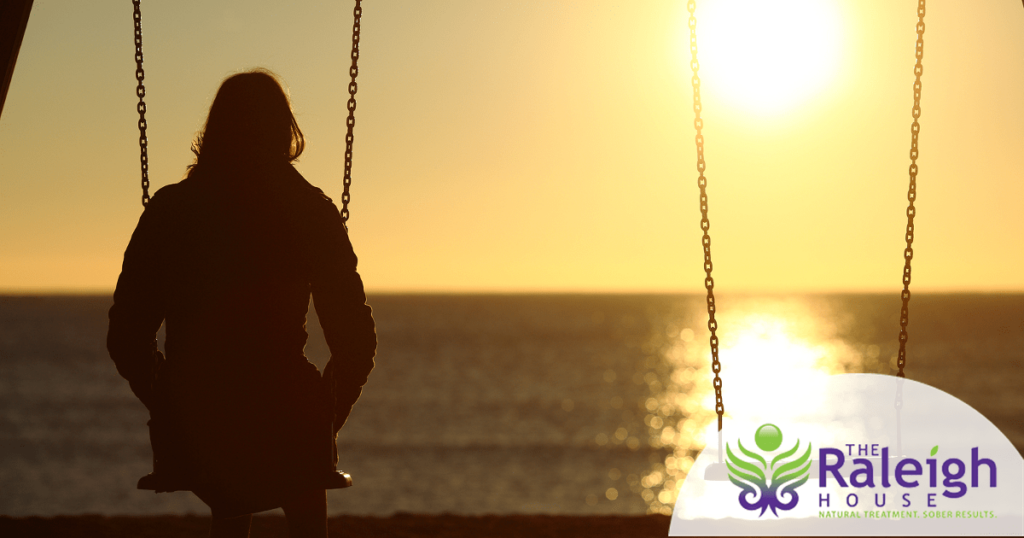 A woman sits on a swing watching the sun set, with an empty swing next to her. 