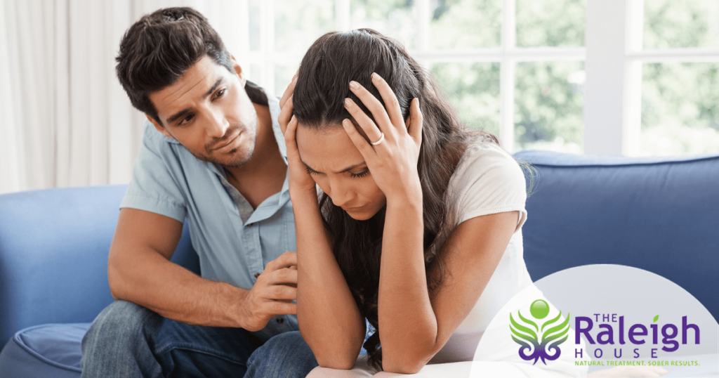A man puts his arm around his wife as they sit on a couch to comfort her.