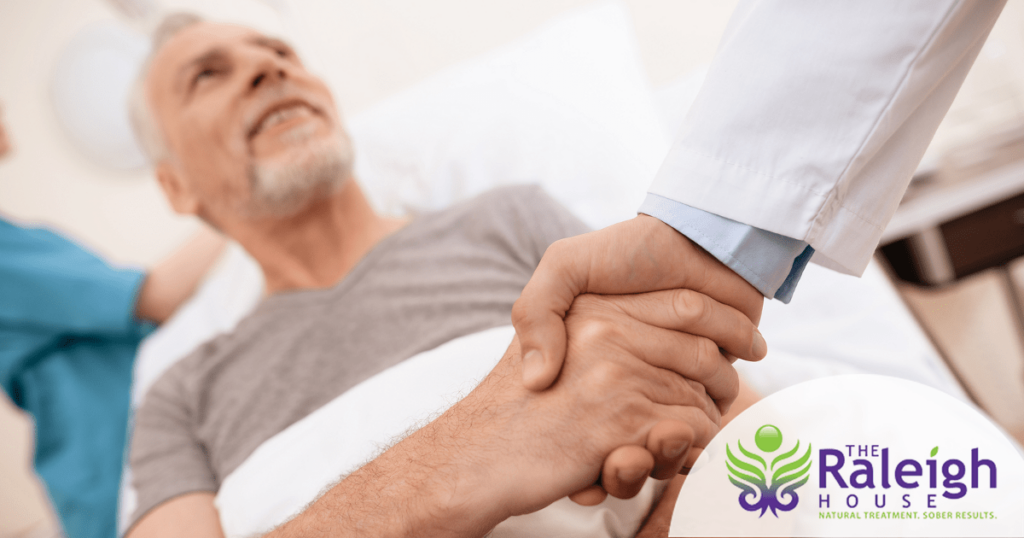 A doctor shakes an older man’s hand as he reclines in his hospital bed.