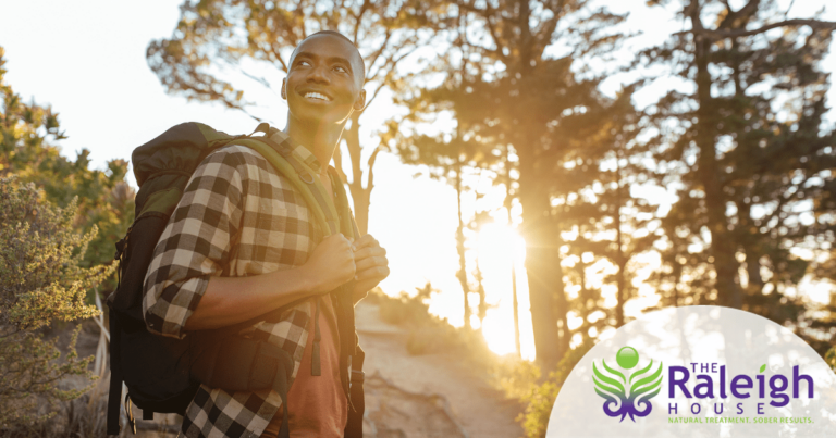 A woman in the middle of a hike sits on a log to take a rest with a big smile on her face.