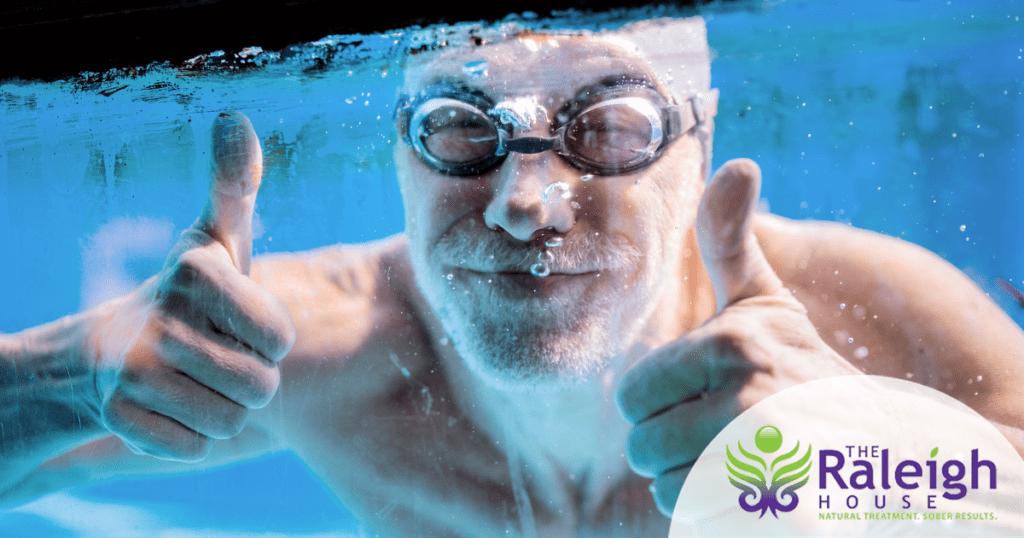 A man wearing goggles in a swimming pool gives two thumbs up from underneath the water. 