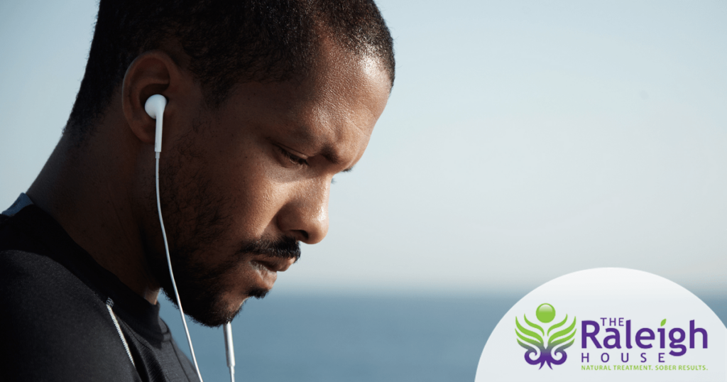An upset young man walks along the waterfront with headphones in his ears.