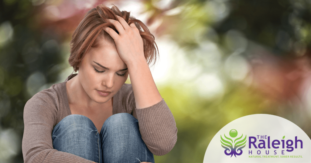 A depressed woman sitting outside runs her hands through her hair.