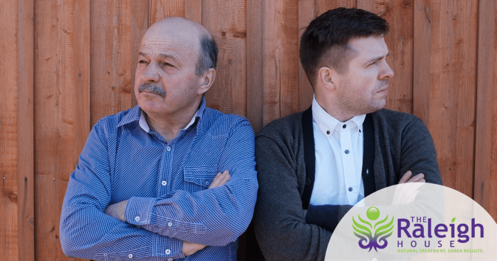 A father and his adult son stand next to each other, arms crossed and looking opposite directions.