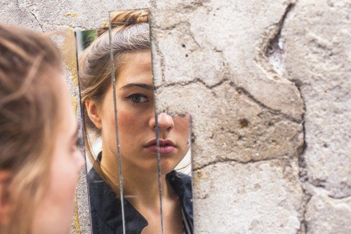 Caucasian woman looking at her self in a broken mirror.