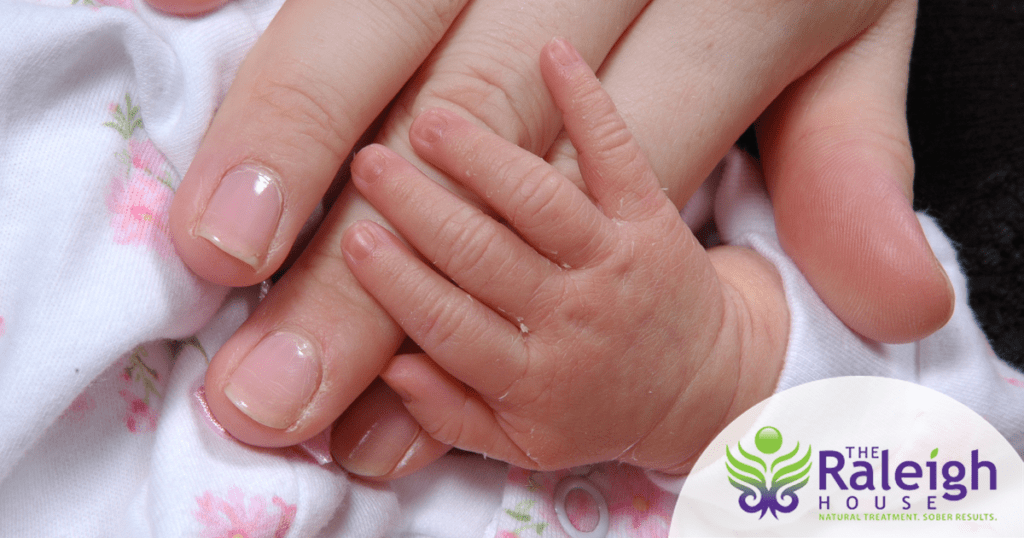 A baby’s hand rests on her mother’s hand.