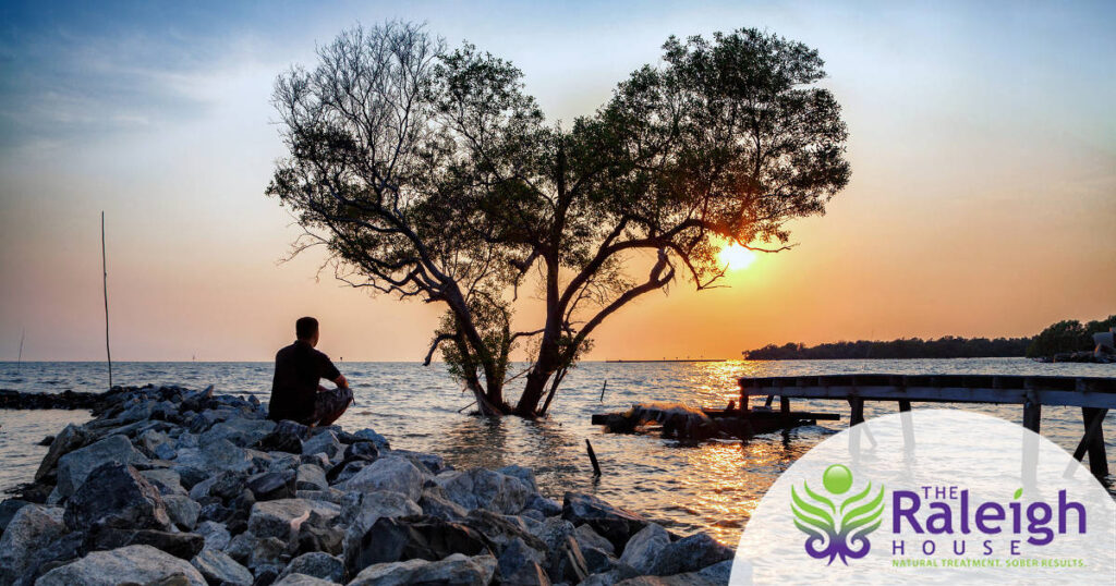 A man sits alone looking out at a lake.