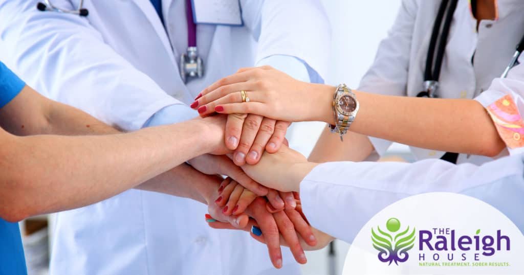 A team of doctors and nurses huddles with their hands together in a show of teamwork.