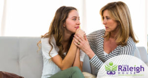 A mother has a heart-to-heart-talk with her teen daughter as they sit on a sofa.