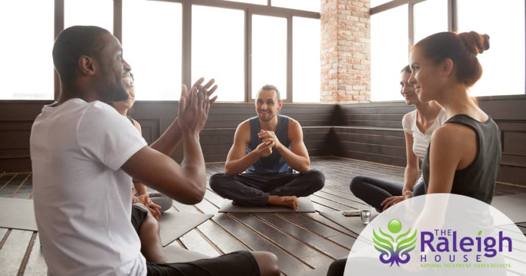 A group of diverse friends chats happily while sitting on yoga mats at a gym.