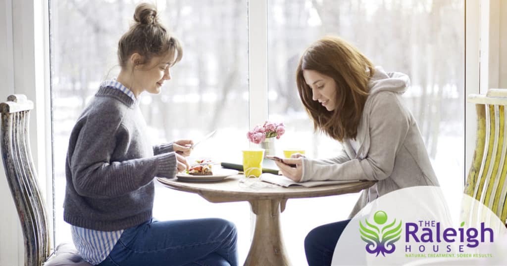 Two young women sit at a table together, eating a snack and studying.