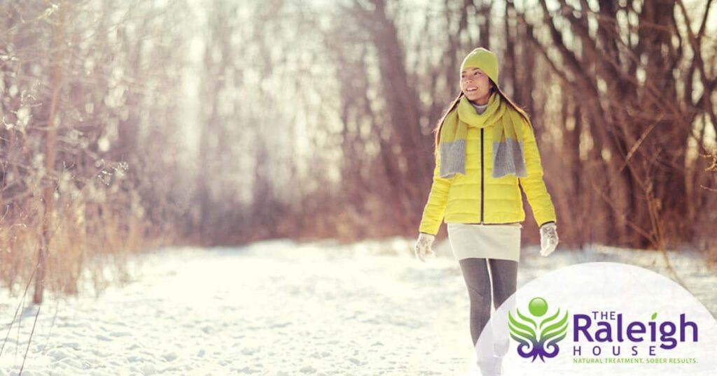 A woman walks outdoors in the snow as the sun shines down on her.