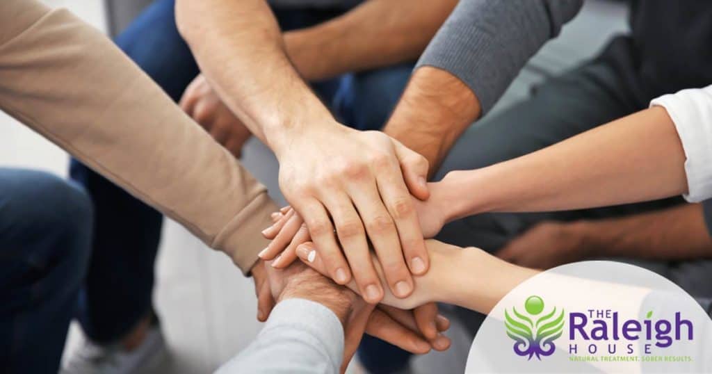 A group of people put their hands together at a group therapy session.