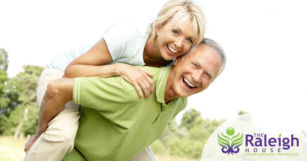 A mature man laughs as he gives his partner a piggyback ride outside.