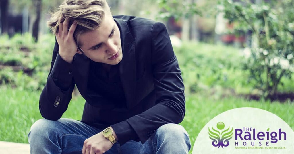 A young man sits alone outside, running his hand through his hair.