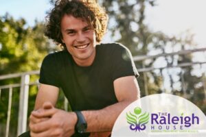 A young man smiles while sitting outside on a nice day.