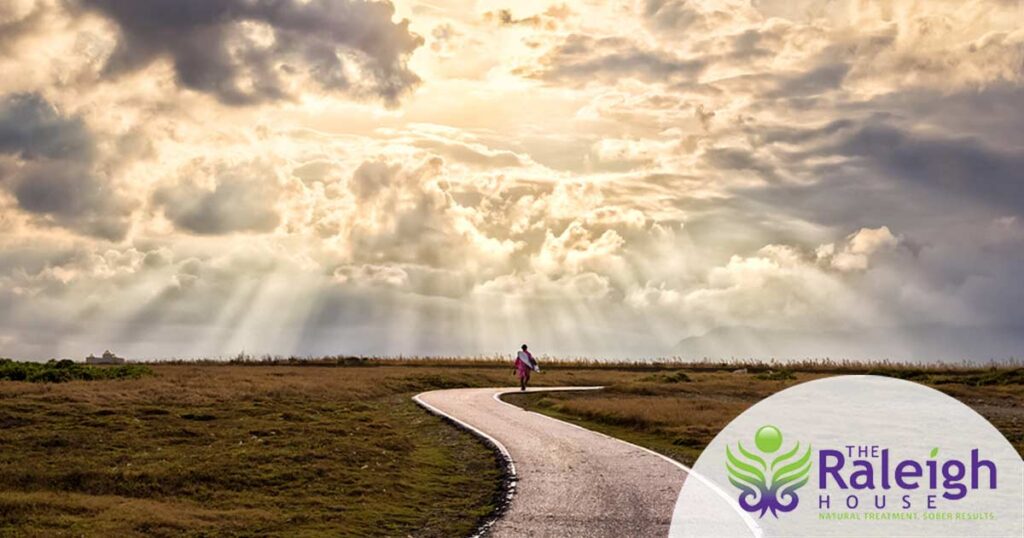 A solitary figure walks along an s-shaped path into the horizon where a cloudy sky and a grassy prairie meet.
