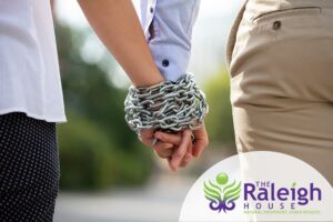 A couple holding hands that are wrapped together by a metal chain.