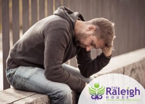 A man sitting on a ledge outside, struggling with his substance abuse and depression.
