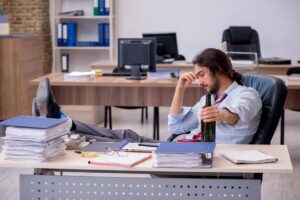 A stressed out white-collar worker drinks at his desk.