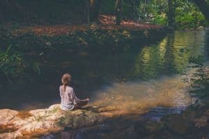 A woman meditating outside in nature, breathing in the fresh air and calming her mind.