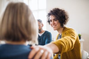 A woman in a sober living meeting, encouraging one of her roommates.