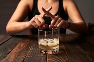 A woman crossing her fingers in front of a glass of alcohol.