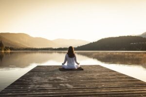 A young woman sits on a pier, practicing meditation during recovery.