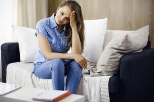 A young woman with anxiety sitting on a couch, struggling to overcome anxiety symptoms.