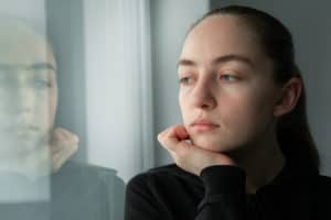 A woman struggling with depression at home looking out the window.