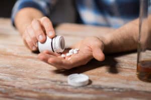 A man’s hands pouring out too many pills because of an addiction.