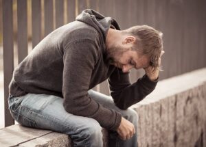 An adult child sitting on an outside staircase struggling with addiction.