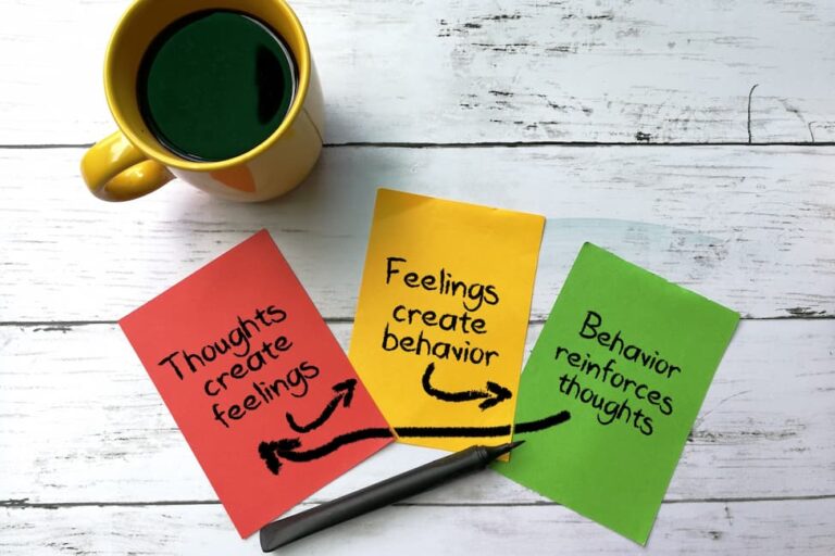 Yellow mug of black coffee and red, yellow, and green sticky notes on wooden table.