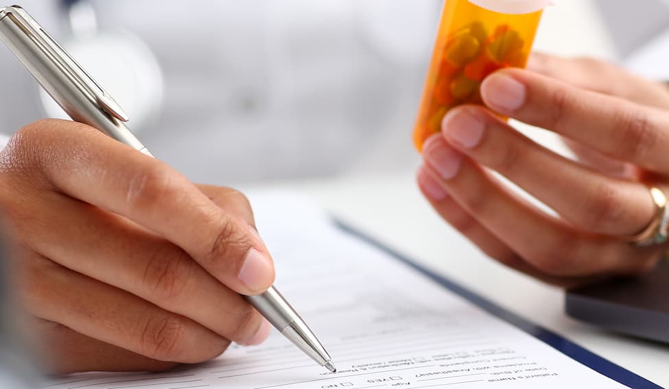 Female doctor's hands holding a bottle of medication and writing a prescription.