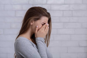 A woman struggling with PTSD with her face in her hands.