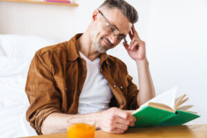 A man sitting at a desk in his room in rehab, reading one of his favorite books.