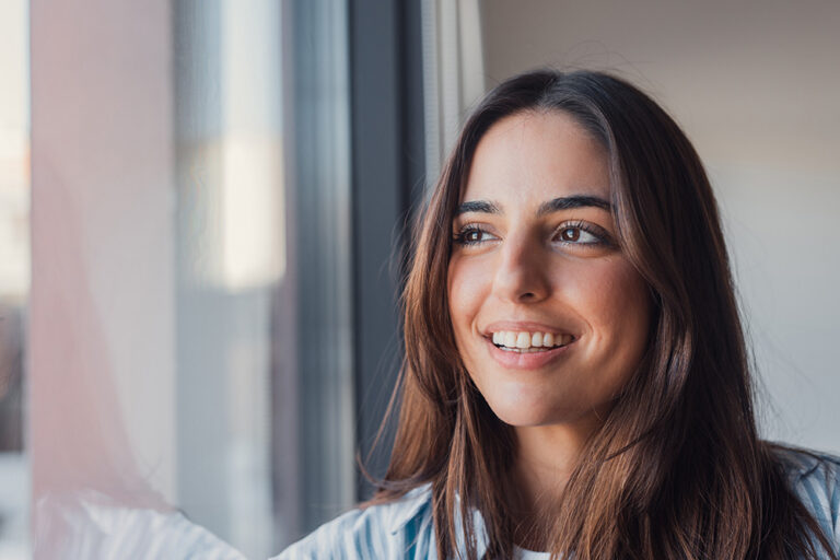 Hopeful young woman looking out window